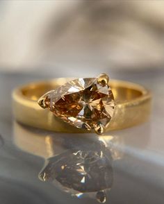 a yellow gold ring with an orange diamond in the center on a reflective surface,