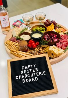 a wooden platter filled with different types of cheese and meats next to a sign that says empty nester charcuterie board