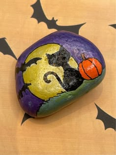 a painted rock with a black cat and pumpkin on it, sitting on a halloween background