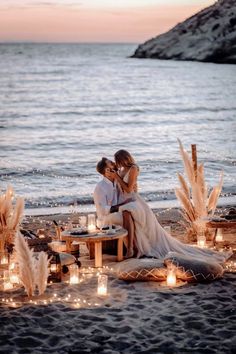 two people sitting on a table with candles in front of them and the water behind them