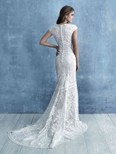 a woman in a white wedding dress standing against a blue wall with her back to the camera