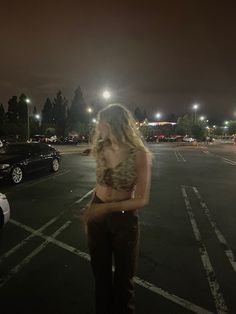 a woman standing in the middle of a parking lot at night with her hands on her hips