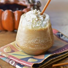 a drink sitting on top of a wooden table next to two orange pumpkins in the background