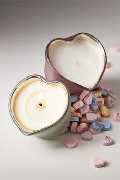 a heart shaped candle sitting next to a container filled with conversation hearts on a white surface