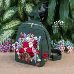 a green backpack with flowers on it sitting in front of some plants