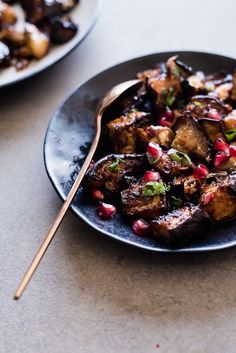 a black plate topped with meat covered in pomegranate and garnish