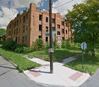 an old brick building on the corner of a street with trees and grass around it