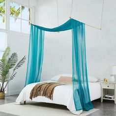 a bed with a blue canopy hanging from it's side in a white room