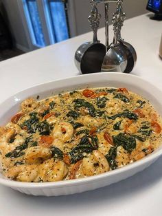 a white dish filled with shrimp and spinach on top of a table next to silverware