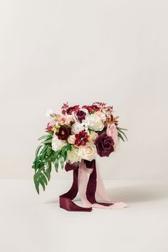 a bouquet of flowers in a vase on a white background with red and pink ribbons