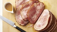 sliced ham sitting on top of a wooden cutting board next to a knife and sauce