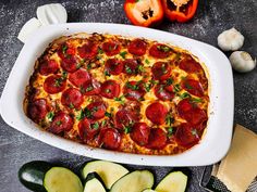 a pizza with pepperoni and cheese in a casserole dish next to sliced zucchini