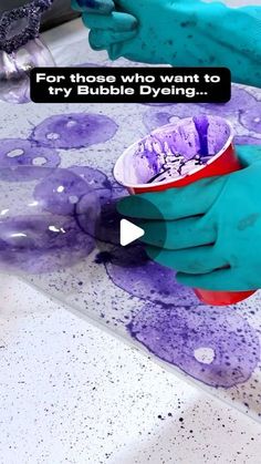 a person in blue gloves is pouring purple liquid into a cup on top of a table