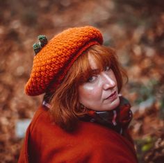 a woman with red hair wearing an orange knitted hat and scarf, looking off to the side