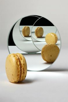 three macaroons are shown in front of a round mirror with the reflection of two macaroons on it