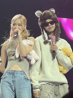 two people standing next to each other with microphones in their hands and one holding a teddy bear