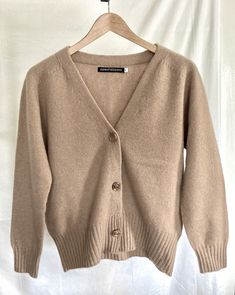 a beige cardigan sweater hanging on a hanger against a white backdrop with a black button down the front