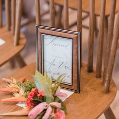 flowers are placed on the side of a wooden chair next to a framed sign that reads,