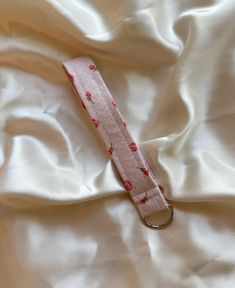 a pink keychain laying on top of a white sheet covered in satin material