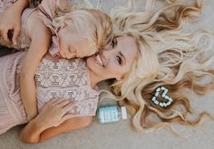 two blonde women laying on the ground with their hair blowing in the wind and smiling