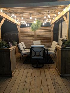 an outdoor patio with lights strung over the table and chairs on the wooden flooring