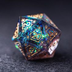 a close up of a colorful dice on a black surface with gold and green designs