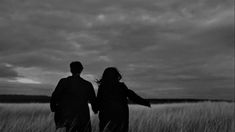 black and white photograph of two people standing in tall grass looking out at the sky