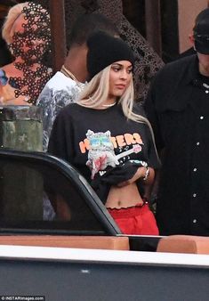 the blonde woman is standing in front of her car and talking to another man who is wearing a black hat