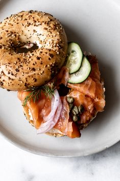 a bagel sandwich with salmon, cucumber and capers on the side