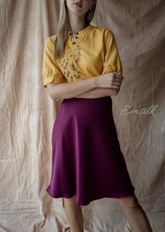 a woman in a yellow shirt and purple skirt posing for the camera with her arms crossed