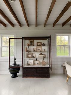 a room with white walls and wooden beams, including an old fashioned cabinet in the center