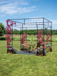 a garden with pink flowers and chairs on the grass in front of an open field