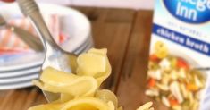 a fork full of pasta on top of a wooden table next to a carton of milk