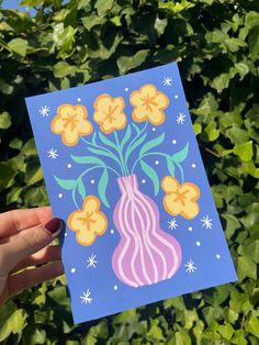 a person holding up a card with flowers on it in front of some leaves and bushes