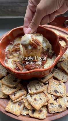 a person dipping some kind of food in a bowl with crackers on the side