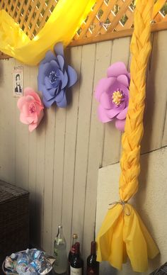 some paper flowers are hanging on the wall next to bottles and wine bottle holders in front of a fence