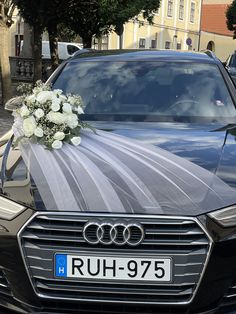 a wedding car decorated with white flowers and ribbon on the hood is parked in front of a building