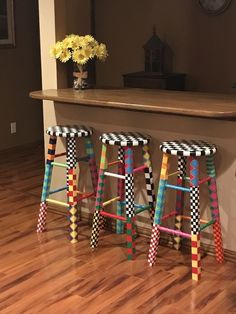 three colorful stools sitting on top of a hard wood floor next to a counter