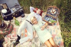 a man and woman laying on a blanket next to an open suitcase in the grass