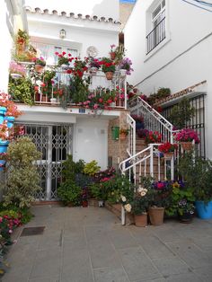 a white house with lots of potted plants and flowers on the balconies