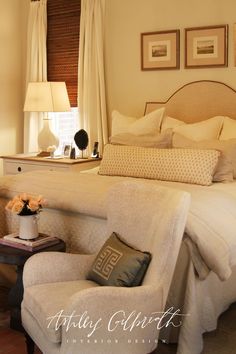 a white bed sitting next to a window with curtains on top of it and a chair in front of it