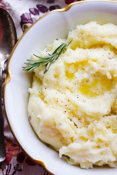 mashed potatoes in a white bowl with a sprig of rosemary