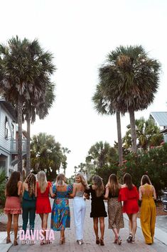 a group of women standing next to each other in front of palm trees and buildings