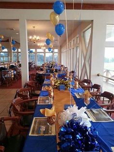 a long table with blue and gold decorations on it, along with balloons in the air