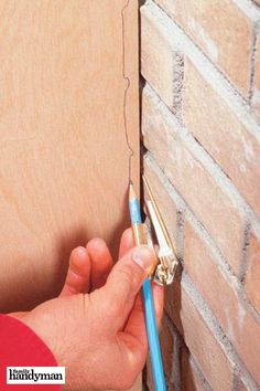 a person is holding a blue pen in front of a brick wall with a hole