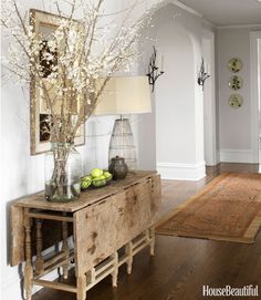 a vase with flowers and fruit on a table in a room that is painted white