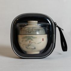 a small black and white container with a handle on the side that holds a teapot