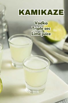 two shot glasses filled with vodka on top of a white tray next to limes