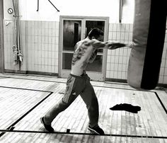 a man standing on top of a hard wood floor next to a punching bag in a gym