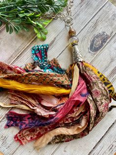 an assortment of scarves and necklaces laid out on a wooden table with greenery